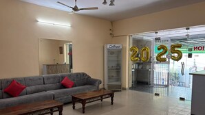 A hotel lobby with a grey sofa, two wooden tables, a ceiling fan, a reception desk, and a refrigerator. - Bagga Vilas (Jaipur)