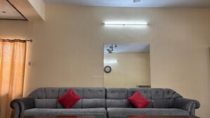 A living room with a grey sofa, two wooden coffee tables, a ceiling fan, a wall-mounted clock, and a large mirror reflecting the room. - Bagga Vilas (Jaipur)