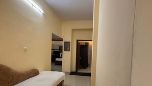 A narrow hallway with a single bed on the left, a door at the end, and a light fixture on the ceiling. - Bagga Vilas (Jaipur)