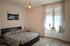 A bedroom with a bed, a hanging light fixture, a window with curtains, and a painting on the wall.