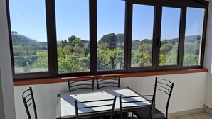 Un comedor con una mesa y sillas, ventanas amplias con vistas a zonas verdes y colinas.