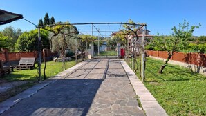 Un sendero de piedra conduce a una entrada con puerta, rodeado de follaje y un cielo azul despejado.