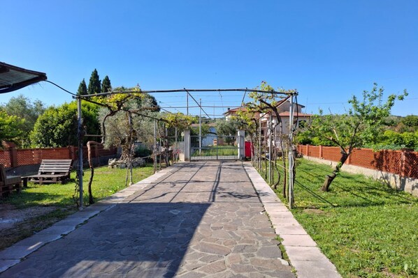 A stone pathway leading to a gated entrance, surrounded by greenery and a clear blue sky.
