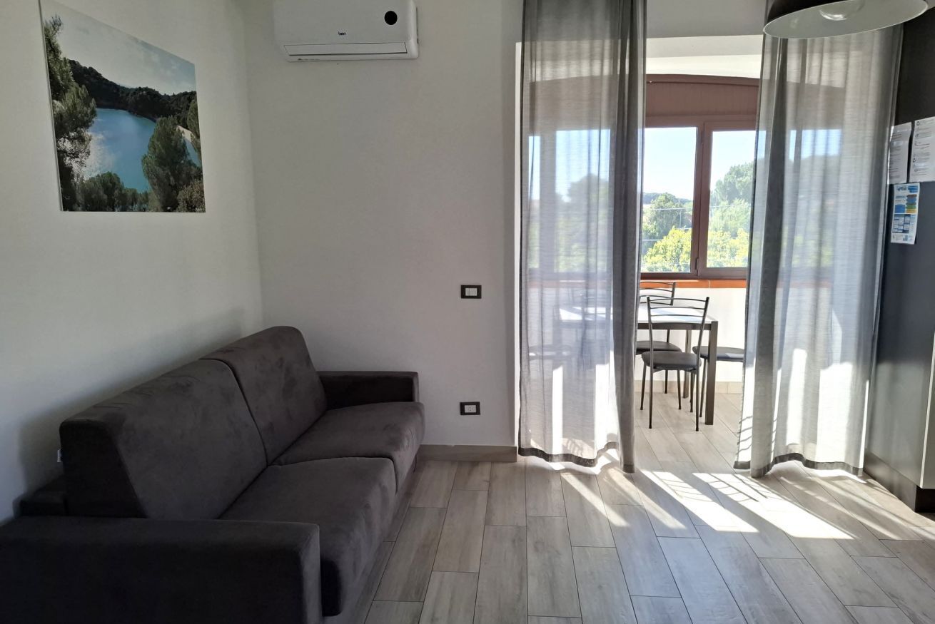 Una sala de estar con un sofá, una zona de comedor con sillas y una mesa, y un ventanal con cortinas.