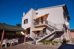 A two-story building with a balcony, outdoor seating, and potted plants.