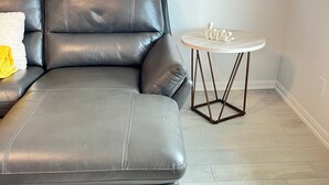 A modern living room with a sectional sofa, a small round table with a 'love' sign, and light-colored wooden flooring. - Ultimate  retreat gateway (Rosharon)