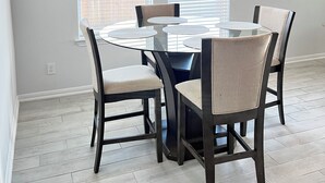 A dining area with a round table and four chairs, large windows with blinds, and a light-colored floor. - Ultimate  retreat gateway (Rosharon)