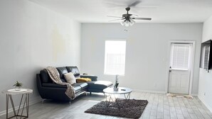 A spacious living room with a grey herringbone floor, a black sofa, a round coffee table, and a ceiling fan. - Ultimate  retreat gateway (Rosharon)