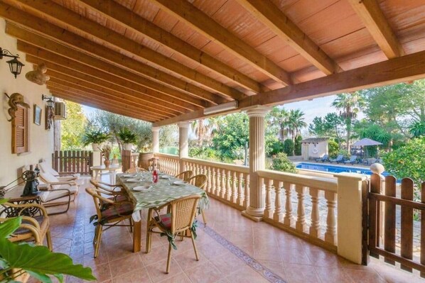 A covered patio with a dining table set for four, surrounded by wicker chairs.