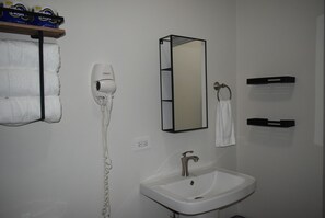 Un baño con lavamanos blanco, secador de pelo, espejo y toallero.