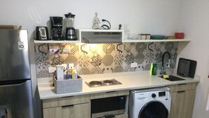 A compact kitchen with a refrigerator, washing machine, and a microwave. There are various kitchen appliances and utensils on the countertop.
