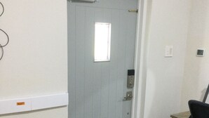 A room with a door, a small window, a desk with a chair, and a trash bin.