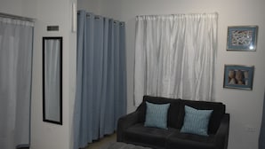 A living room with a dark sofa, two patterned cushions, a grey ottoman, and a mirror on the wall.