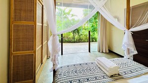 A room with a four-poster bed, a patterned rug, and a view of lush greenery outside. - Samudra Damai Villas (Pecatu)