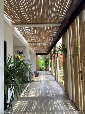 Un pasillo cubierto con columnas de bambú, plantas en macetas y una zona de estar.