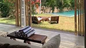 A covered outdoor seating area with a pool view, bamboo ceiling, and lush greenery. - Samudra Damai Villas (Pecatu)