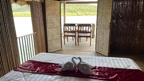 Una habitación con una cama, un edredón rojo y dos almohadas con forma de cisne. En el fondo, se ve una mesa de madera y sillas.