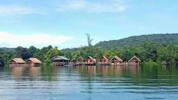 Una serie de casas flotantes de madera sobre un lago tranquilo, rodeadas de exuberante vegetación y colinas.