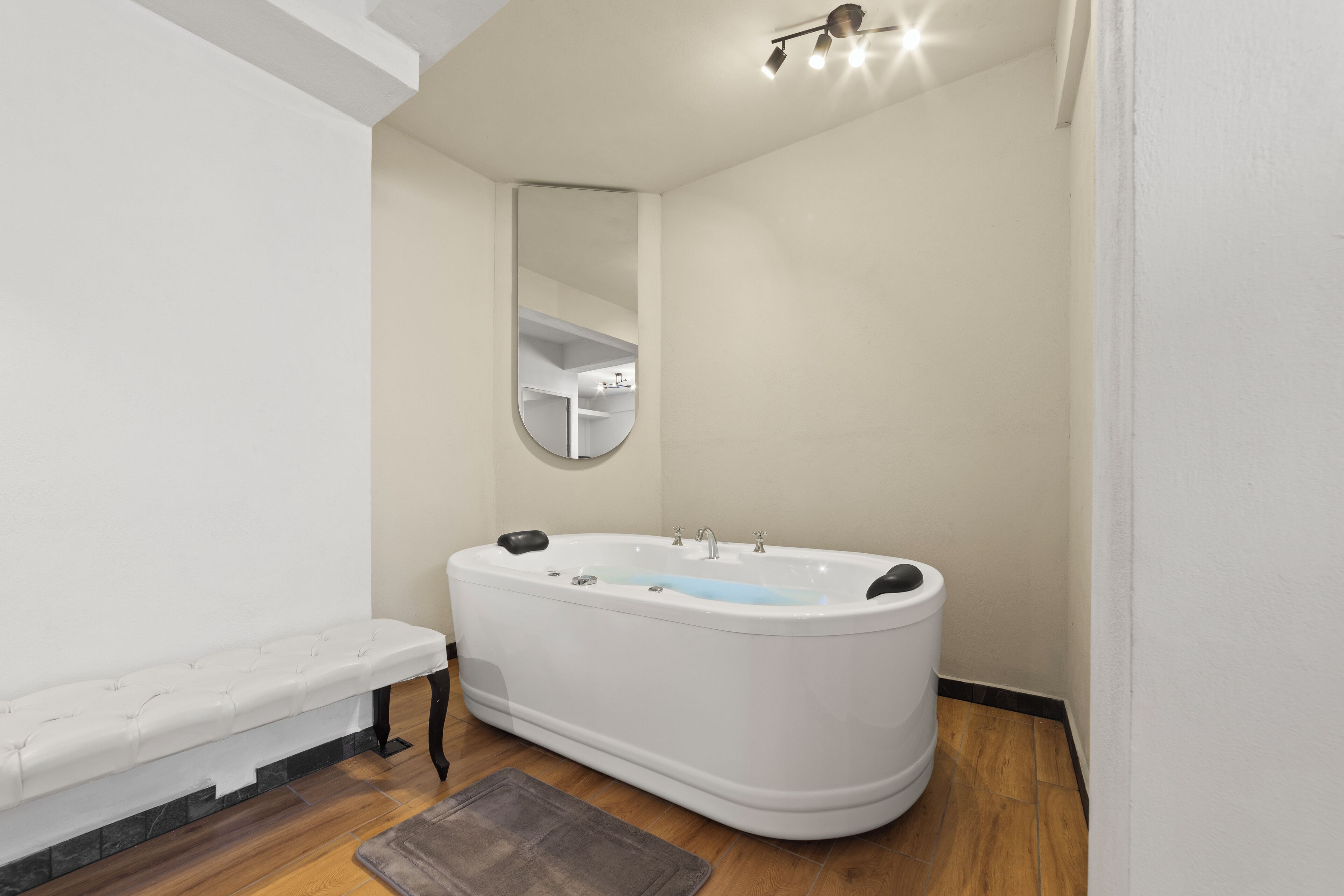 A modern bathroom with a freestanding bathtub, a bench, and a mirror.