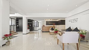 A modern hotel lobby with a reception desk, seating area, and a staircase leading to other floors. - Hotel Boutique Árbol de la Vida (Taxco)