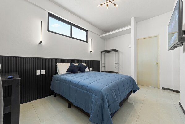 A bedroom with a bed, a desk, a window, and a door.