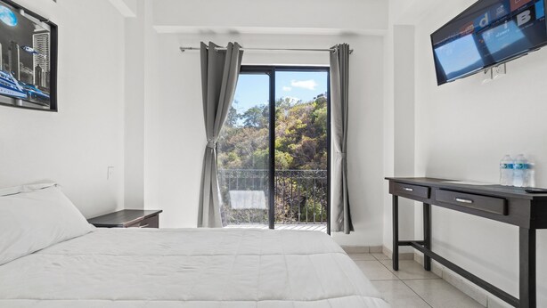 A bedroom with a bed, a desk, a TV, and a balcony with curtains. - Hotel Boutique Árbol de la Vida (Taxco)