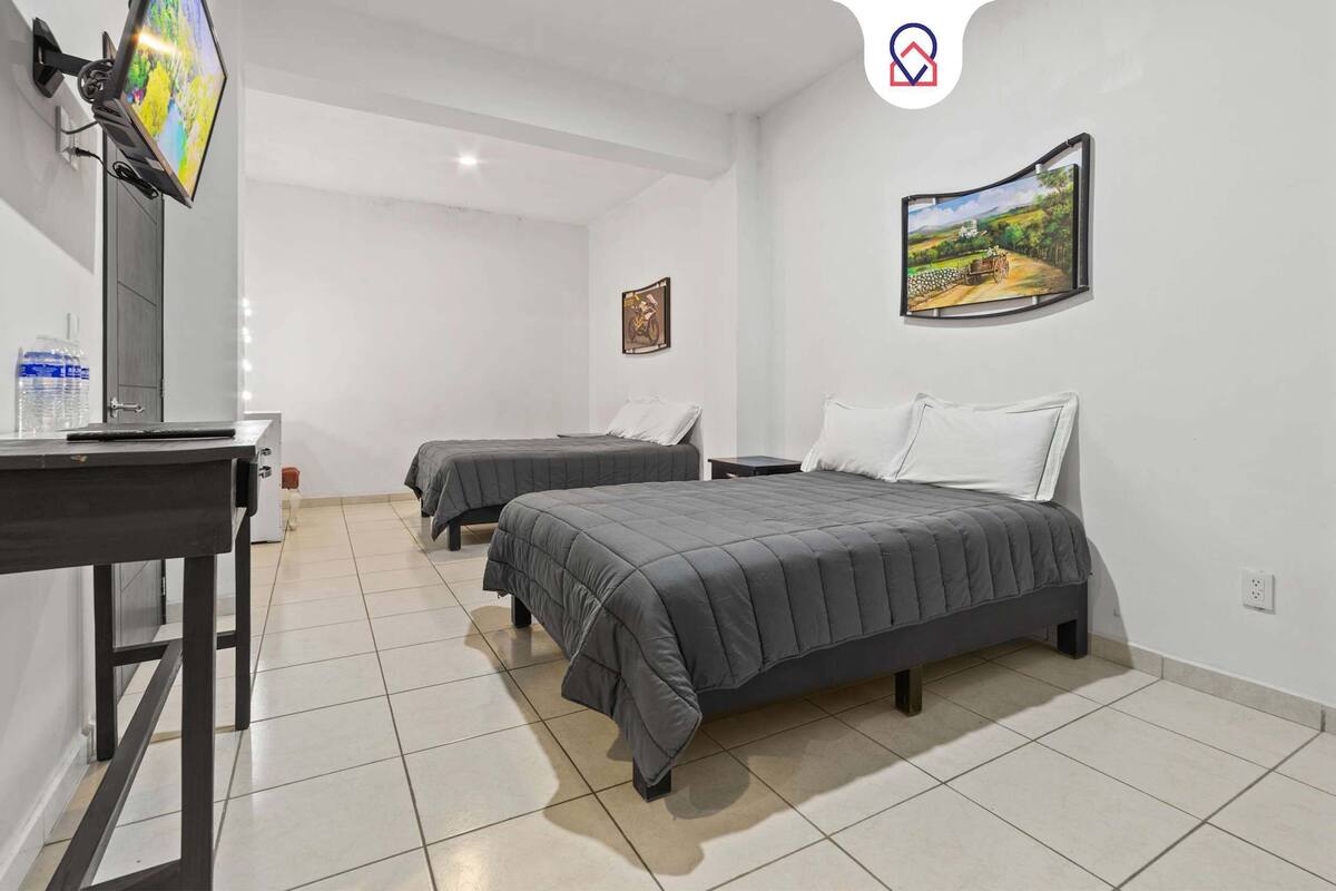 Une chambre d’hôtel avec deux lits, un bureau, un téléviseur fixé au mur et un tableau.