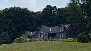 Een groot, donker huis met een schuin dak, omgeven door een verzorgd gazon en weelderige bomen.