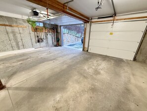 Un garaje con suelo de concreto, vigas de madera, ventilador de techo y pared de piedra.