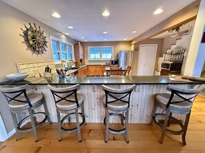 Une cuisine dotée d’un îlot central, de tabourets de bar en bois et d’une horloge décorative au mur.