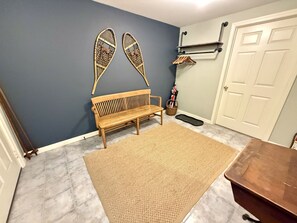 Une pièce comprenant un banc en bois, un tapis tissé, une étagère fixée au mur et une porte.
