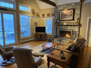 Un salon chaleureux avec une cheminée en pierre, des meubles en cuir et une grande fenêtre donnant sur un espace extérieur enneigé.