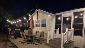 Een overdekt terras met een tafel, stoelen, een barbecue en sfeerverlichting.