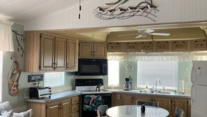 Een kleine keuken met houten kastjes, een magnetron, een fornuis en een eethoek met een tafel en stoelen.