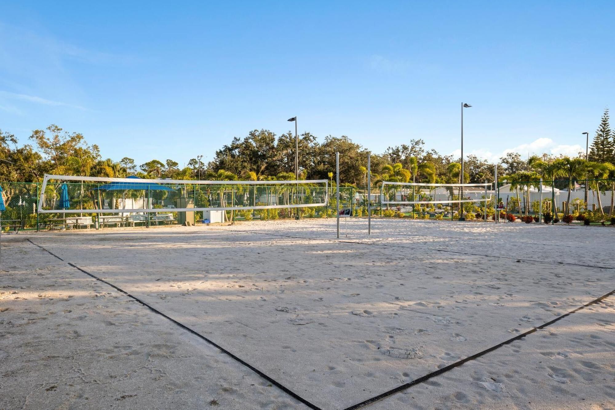 Uma quadra de voleibol de praia vazia, com rede, bancos e uma estrutura azul ao fundo.