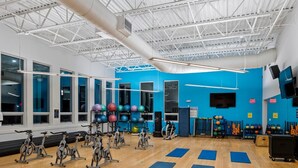 Een sportschool met spinningfietsen, matten en diverse fitnessapparaten.