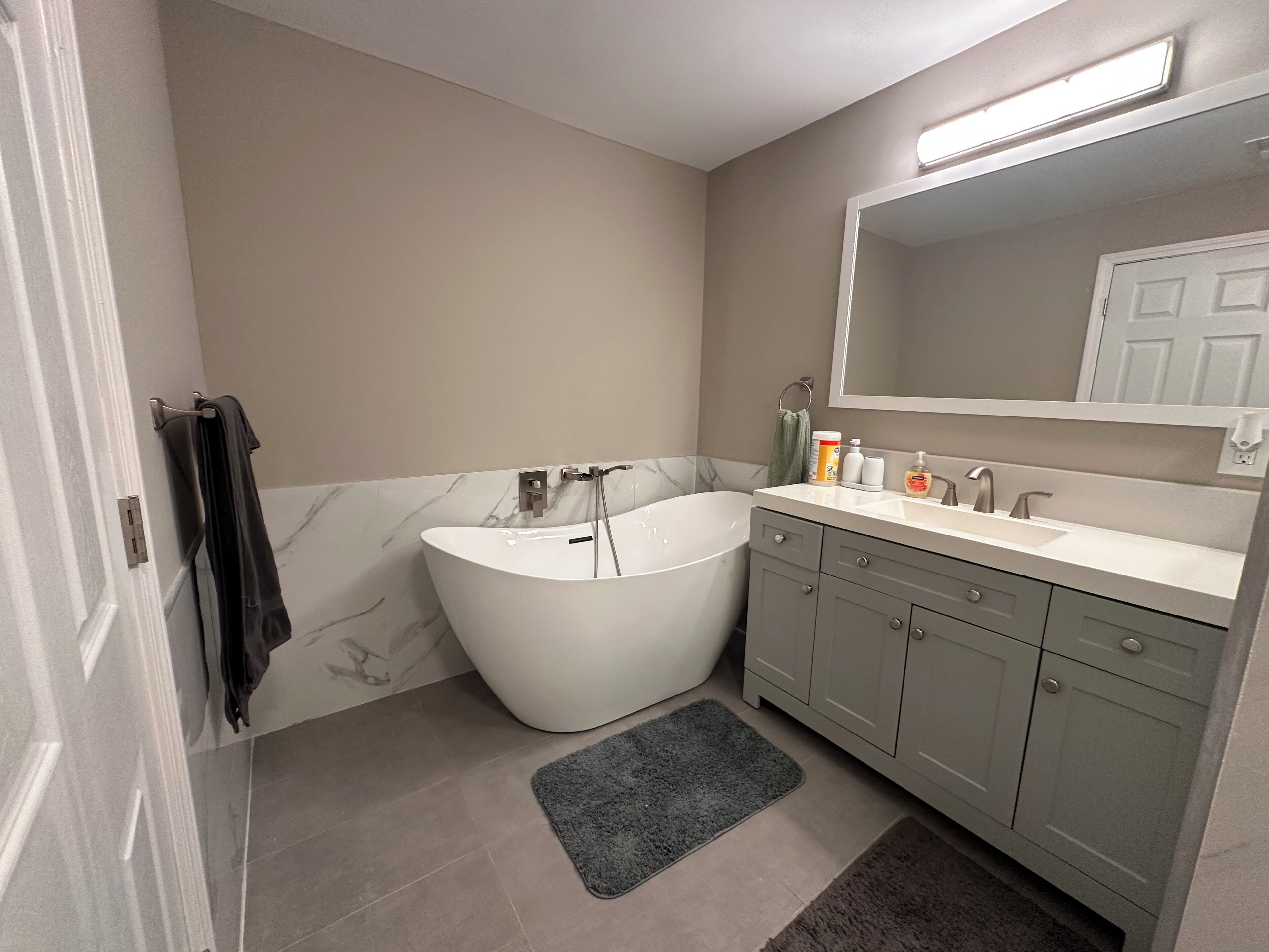 Ein modernes Badezimmer mit einer freistehenden Badewanne, einem Waschtisch mit Spiegel und einem Handtuchhalter.