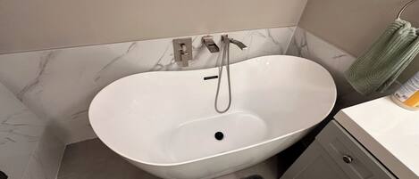 A bathroom with a freestanding bathtub, a towel rack with a towel, and a bottle of shampoo.