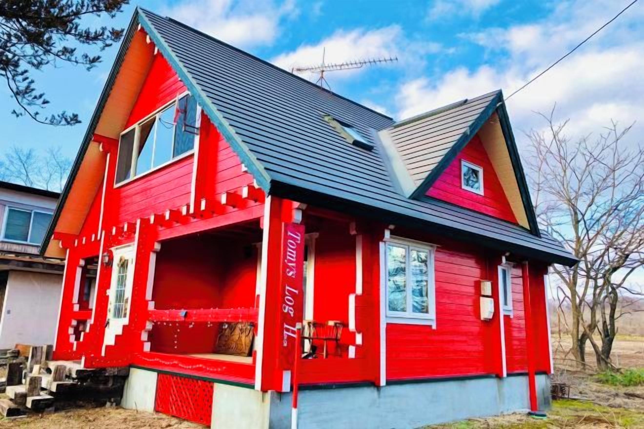 A red house with a gabled roof, a front porch, and a small front yard.