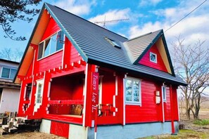Een rood huis met een puntgevel, een veranda en een kleine voortuin.