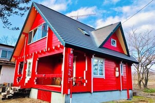 A red house with a gabled roof, a front porch, and a small front yard.