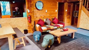 L’intérieur d’un chalet accueillant, avec un canapé en bois, une table ronde et un petit tabouret.
