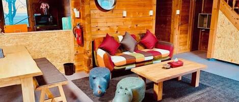 Interior acogedor de una cabaña con un sofá de madera, una mesa redonda y un taburete pequeño.