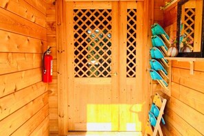 Eine Holzhütte mit einem an der Wand befestigten Feuerlöscher, einer Tür mit Gittermuster und einem Gestell mit blauen Taschen.