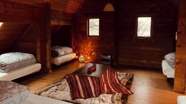 A cozy cabin with wooden walls, two windows, a central table, and several mattresses.