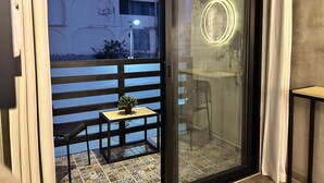 Une pièce dotée d’une porte-fenêtre coulissante donnant sur un balcon carrelé, avec une petite table et une plante.