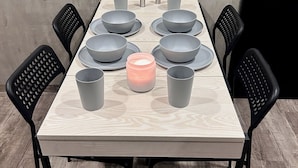 Une table à manger dressée avec des bols, des assiettes et des tasses de couleur grise, et une bougie rose placée au centre.