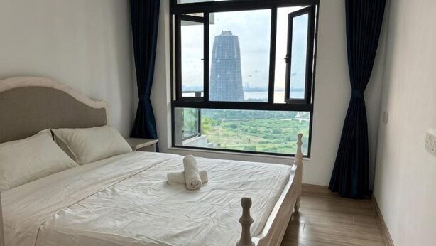 A bed with a headboard, a window with curtains, and a view of a building and greenery. - Cozy 2B1R 4pax condo Forest City 3A-3202 (Gelang Patah)