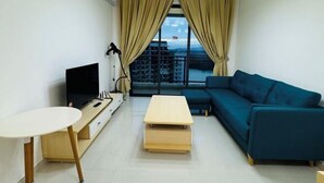 A modern living room with a TV, a sofa, a small table, and a view of buildings through large windows. - Cozy 2B1R 4pax condo Forest City 3A-3202 (Gelang Patah)