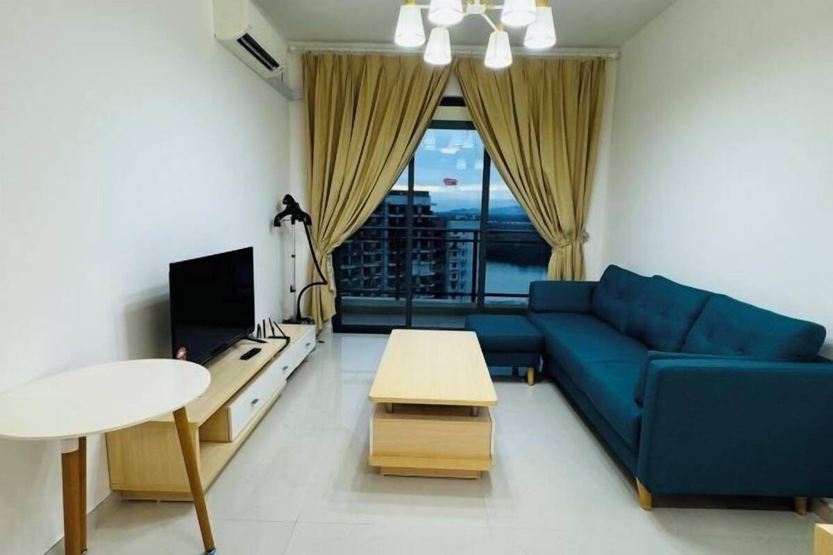 A modern living room with a TV, a sofa, a small table, and a view of buildings through large windows.